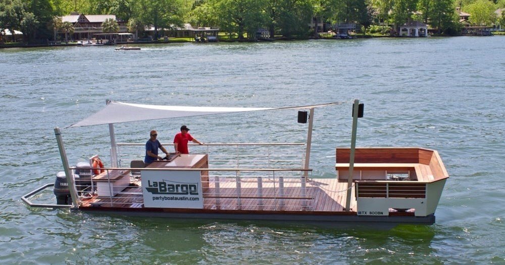 LaBarge party boat with wooden deck and canopy cruising on Lake Austin with people onboard.