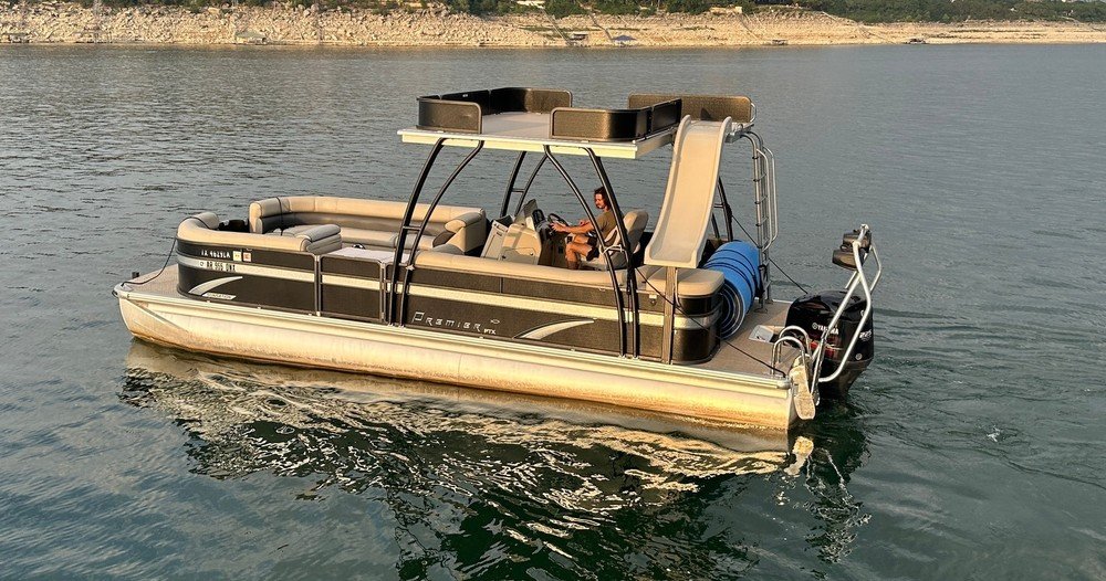 Premier pontoon boat with slide and shaded top cruising across calm lake waters.