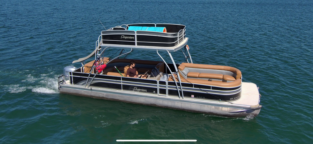 Premier pontoon boat with tan seating and shaded upper deck cruising on lake.
