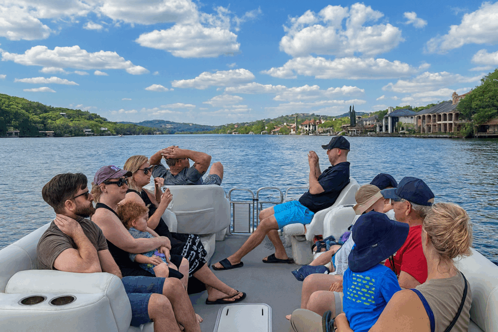 Group of families relaxing on a pontoon boat ride, enjoying scenic lake views under a blue sky with scattered clouds.
