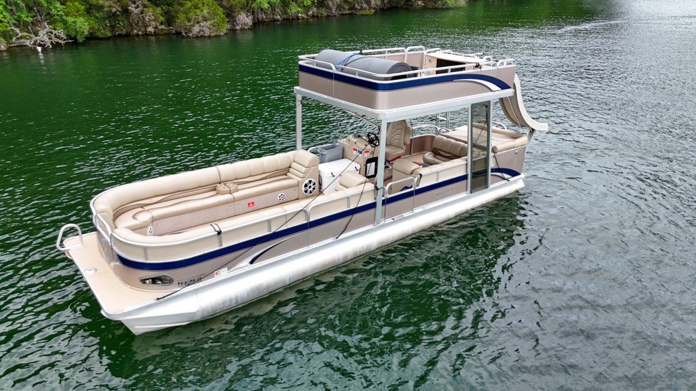 Spacious Avalon pontoon boat with tan seating and upper deck slide on clear lake water.