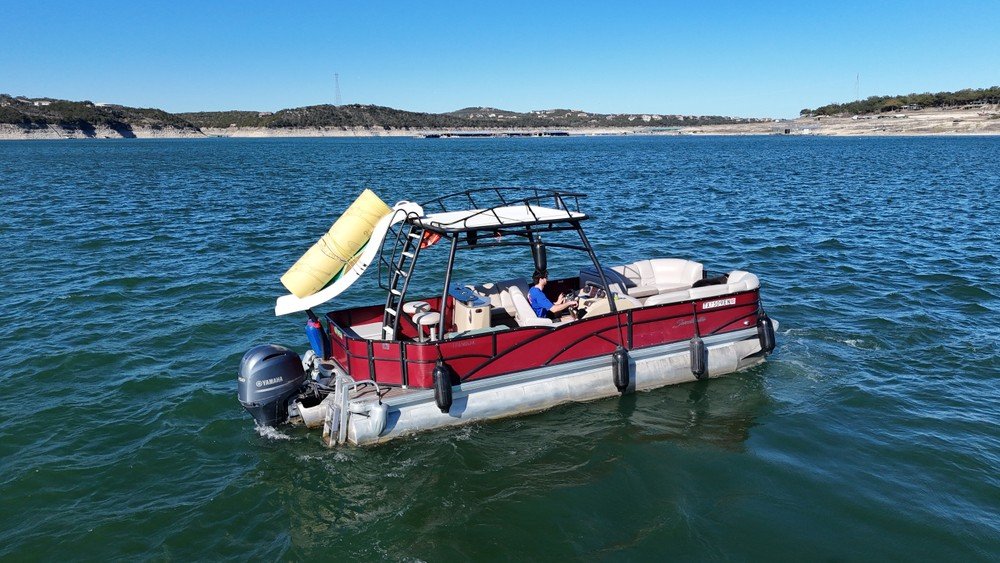 Red pontoon boat with sunshade and rolled-up floating mat cruising across Lake Travis.
