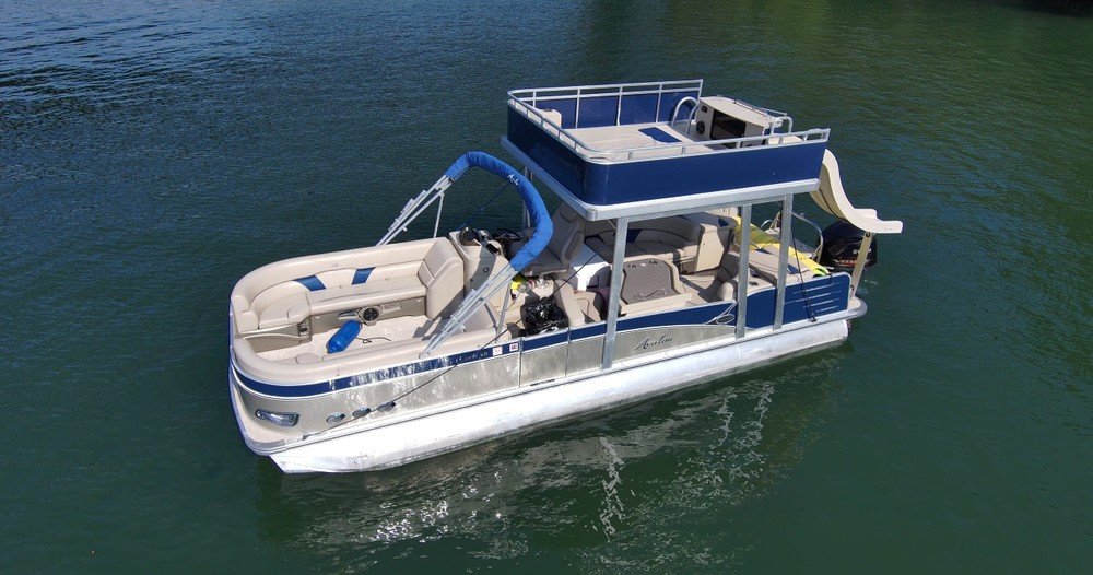 Avalon pontoon boat with upper deck and waterslide floating on calm lake water.
