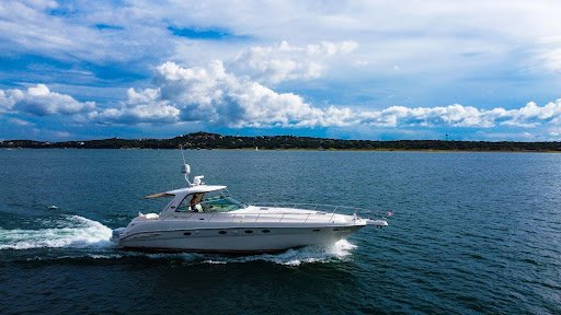 Luxury white yacht cruising across open water under blue sky with shoreline in the background.